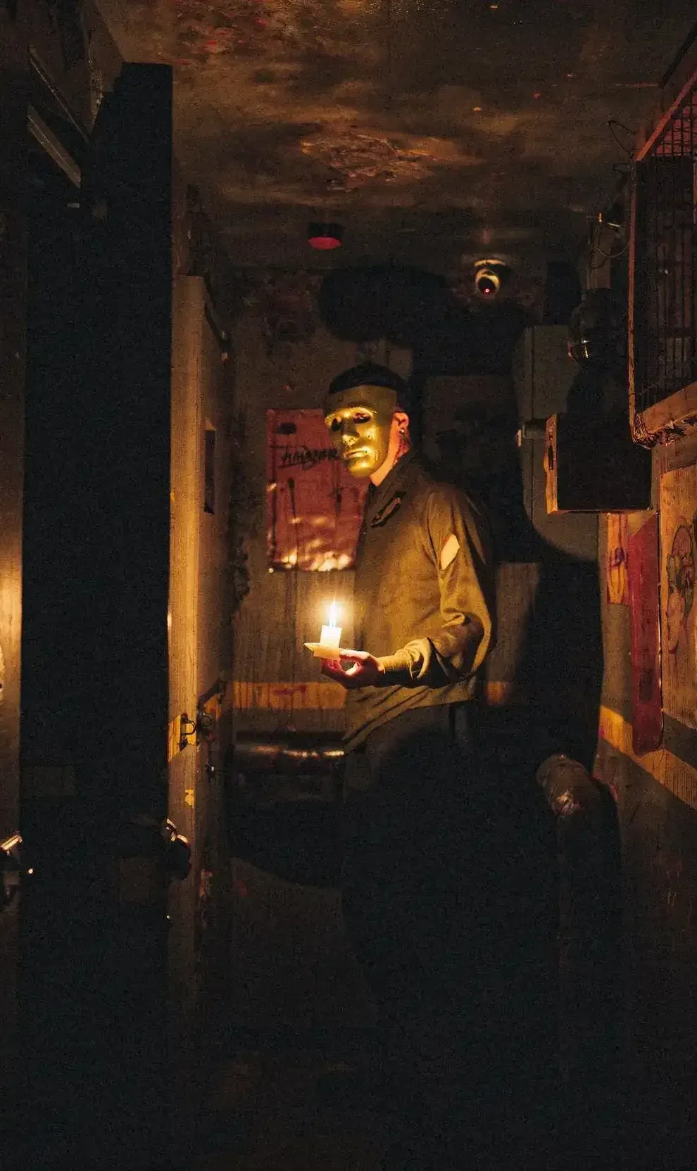 Personnage masqué dans un couloir sombre éclairé par une bougie, tenant un objet, ambiance mystérieuse et immersive d'un escape game ou d'une scène d'horreur