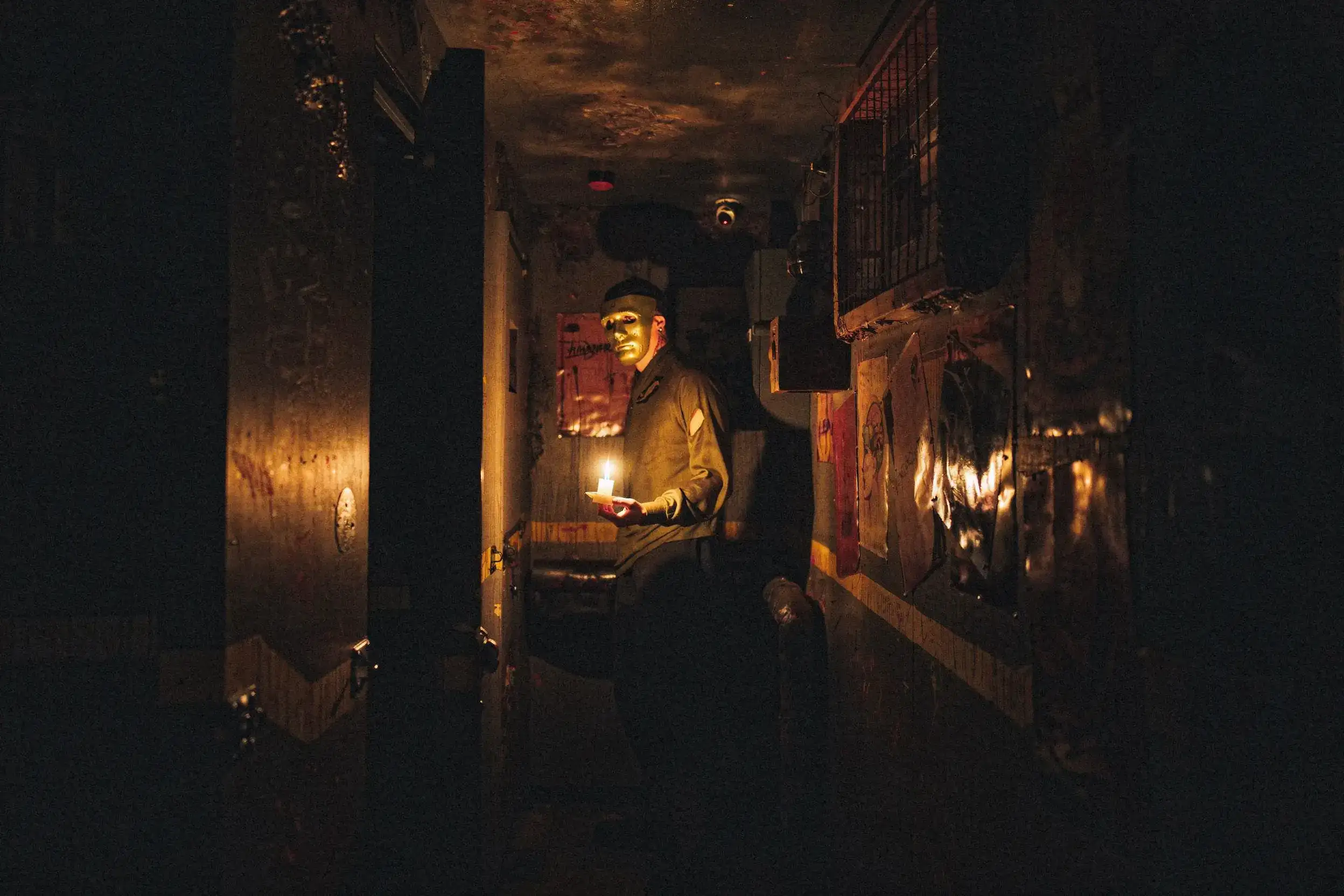 Personnage masqué dans un couloir sombre éclairé par une bougie, tenant un objet, ambiance mystérieuse et immersive d'un escape game ou d'une scène d'horreur