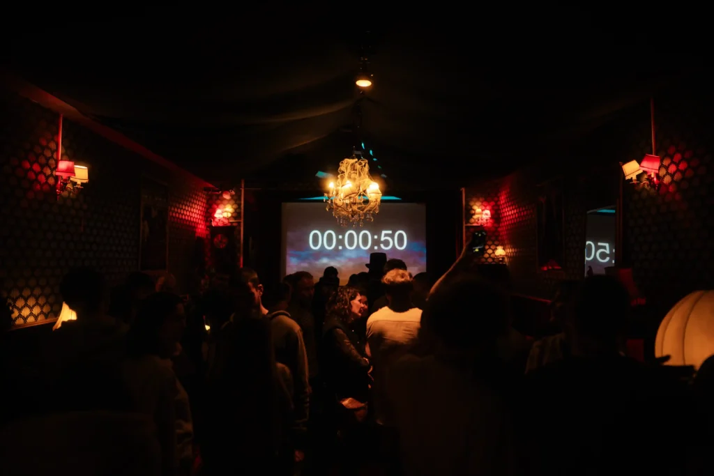 Groupe de personnes dans une pièce faiblement éclairée, avec un écran affichant un compte à rebours à 00:00:50, décorations murales rouges et lumières suspendues.